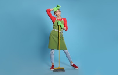 Young housewife with broom on light blue background