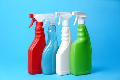 Photo of Spray bottles of detergents on light blue background. Cleaning supplies