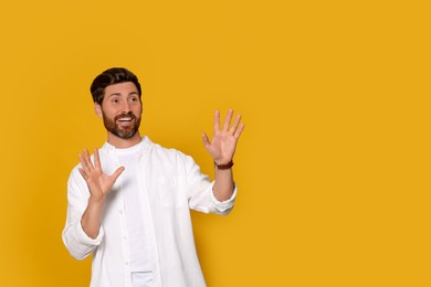 Photo of Portrait of emotional bearded man with open hands on orange background. Space for text