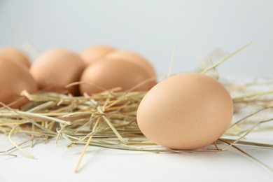 Raw chicken egg and decorative straw on white table, closeup