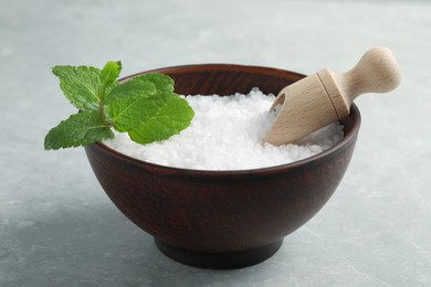 Natural sea salt in wooden bowl, scoop and mint on light grey marble table