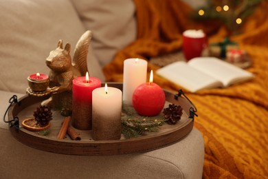 Tray with beautiful burning candles and Christmas decor on sofa at home