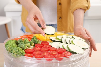Woman putting cut zucchini into fruit dehydrator machine in kitchen, closeup