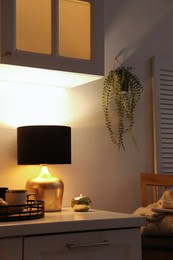 Photo of Stylish lamp, cups and croissant on white cabinet in room. Interior element