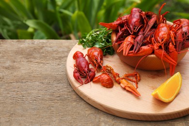 Photo of Delicious red boiled crayfish and orange on wooden table. Space for text