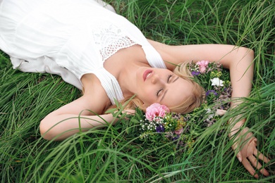 Photo of Young woman wearing wreath made of beautiful flowers on green grass
