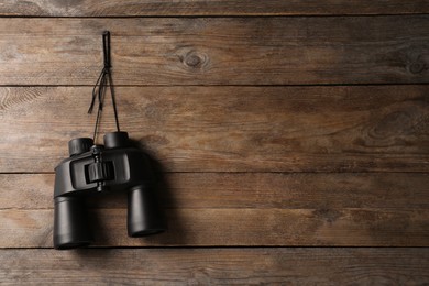 Modern binoculars hanging on wooden wall, space for text
