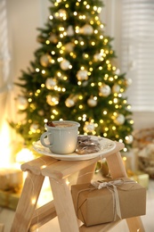 Tasty hot drink and cookies in room with Christmas tree