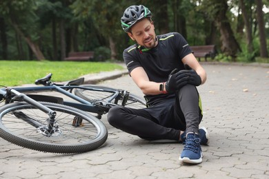 Man with injured knee near bicycle outdoors