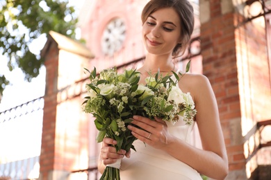 Gorgeous bride in beautiful wedding dress with bouquet near church