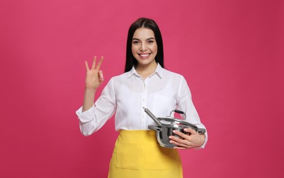 Young housewife with pan on pink background