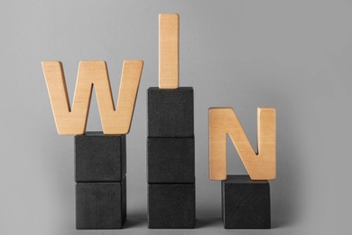Word WIN made with wooden letters on toy blocks against grey background. Victory concept