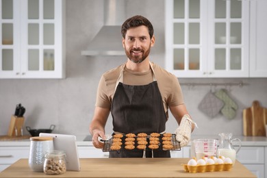Photo of Man holding grid with freshly baked cookies in kitchen. Online cooking course