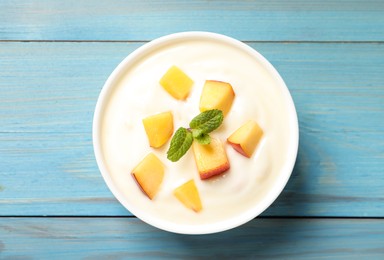 Delicious yogurt with fresh peach and mint on light blue wooden table, top view