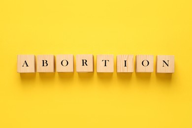 Word Abortion made of wooden cubes on yellow background, flat lay