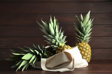 Photo of Bag with fresh juicy pineapples on wooden table