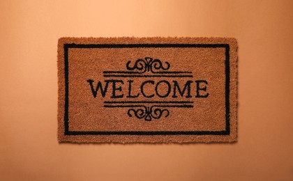 Photo of Doormat with word Welcome on brown background, top view