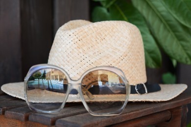 Stylish hat and sunglasses on wooden table, closeup. Beach accessories