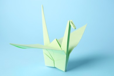 Photo of Origami art. Handmade paper crane on light blue background, closeup
