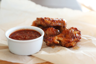 Delicious chicken wings with sauce on wooden board, closeup