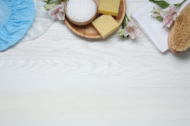 Flat lay composition with shower caps and toiletries on white wooden background. Space for text