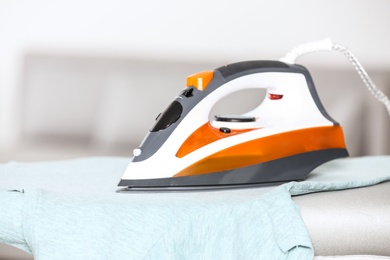 Modern electric iron and clean t-shirt on board indoors