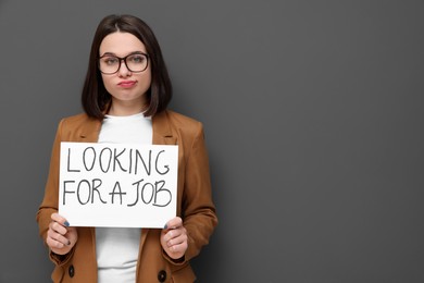 Photo of Upset young unemployed woman holding sign with phrase Looking For A Job on grey background. Space for text