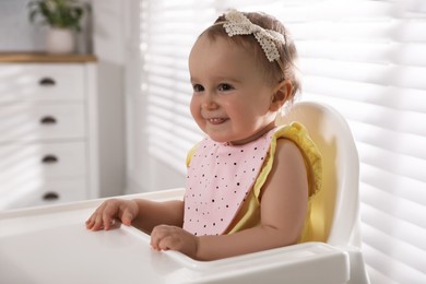 Cute little baby wearing bib in highchair at home