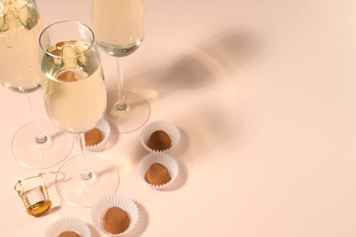 Glasses of delicious sparkling wine and chocolate truffles on pale pink background. Space for text