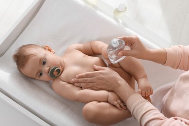 Mother massaging her cute baby with oil on changing table, above view