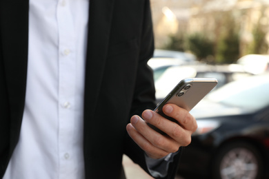 Businessman ordering taxi with smartphone on city street, closeup