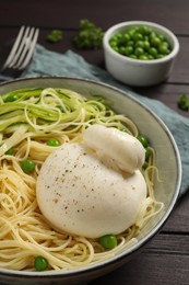 Photo of Bowl of delicious pasta with burrata, peas and zucchini on wooden table, closeup