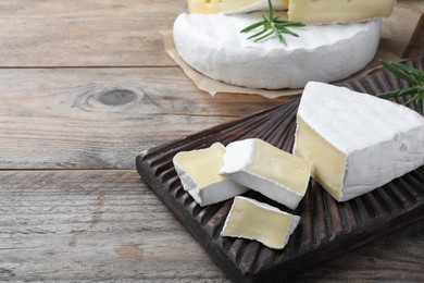 Tasty cut brie cheese with rosemary on wooden table, space for text