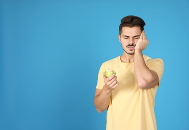 Emotional young man with sensitive teeth and apple on color background. Space for text