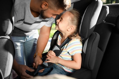 Father fastening his daughter with car safety seat belt. Family vacation