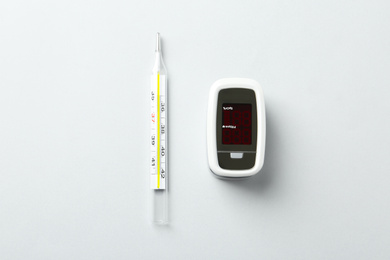 Photo of Modern fingertip pulse oximeter and mercury thermometer on white background, flat lay