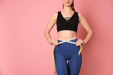 Happy woman in sportswear measuring waist with tape on pink background, closeup. Space for text