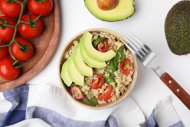 Photo of Delicious quinoa salad with tomatoes, avocado slices and spinach leaves served on white table, flat lay