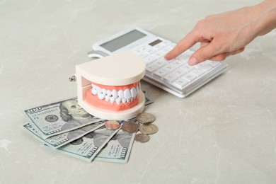 Woman using calculator near educational dental typodont model and money at light grey table, closeup. Expensive treatment