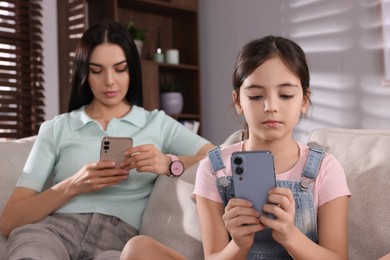 Internet addiction. Mother and her daughter with smartphones on sofa in living room