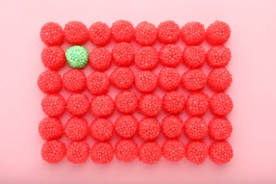 Delicious green gummy raspberry candy among red ones on pink background, flat lay