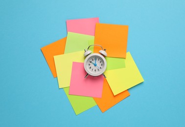 Alarm clock and blank reminder notes on light blue background, flat lay