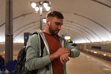Young man with backpack and earphones waiting for train at subway station. Public transport