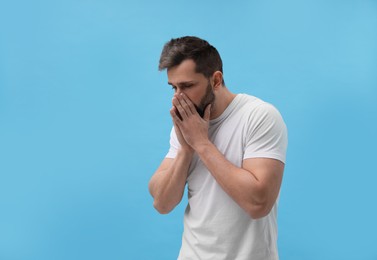 Man sneezing on light blue background. Cold symptoms