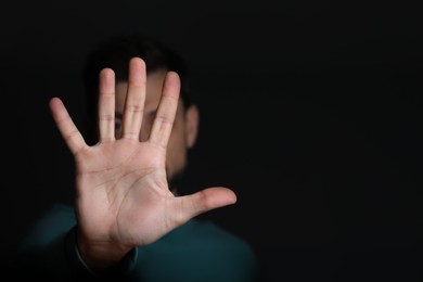 Photo of Man showing stop gesture against black background, focus on hand. Space for text