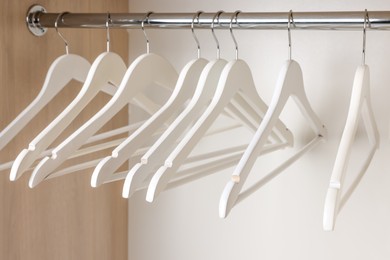 Photo of Set of wooden clothes hangers on wardrobe rail, closeup