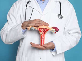 Doctor demonstrating model of female reproductive system on light blue background, closeup. Gynecological care