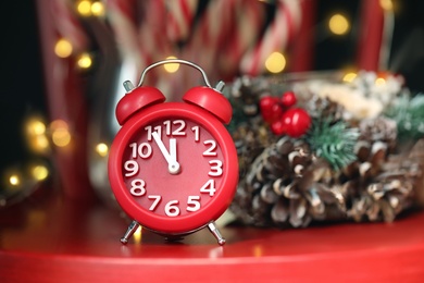 Alarm clock and decor on red table against blurred Christmas lights. New Year countdown