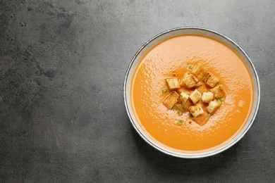 Tasty creamy pumpkin soup with croutons in bowl on grey table, top view. Space for text