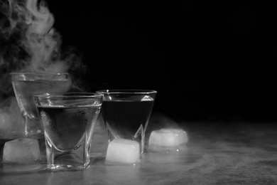 Vodka in shot glasses with ice on table against black background, space for text